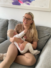 Woman holding a baby on a couch with a colorful abstract painting in the background in her mocha cotton breastfeeding pyjajams