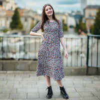 Stylish Mum with hand on hip with rainbow leopard print breastfeeding dress. She has long dark here and is posing confidently. She is also black boots and is stood in on a pavement on a street.