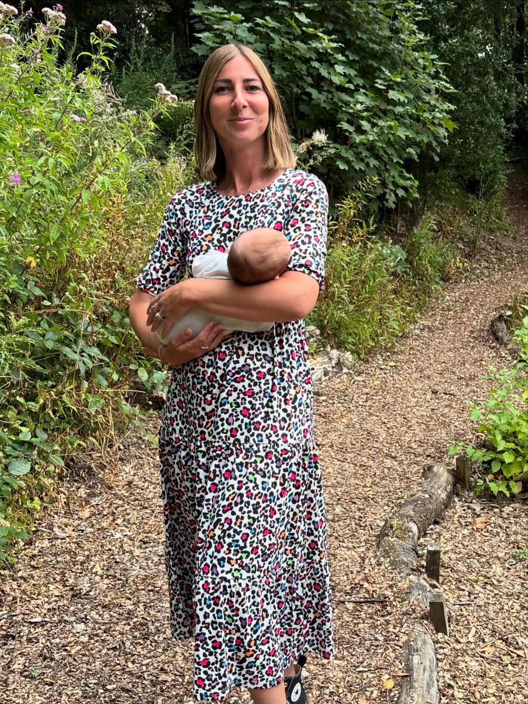 Woman in a floral breastfeeding dress holding a baby outdoors in a garden setting