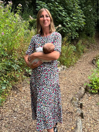 Woman in a floral breastfeeding dress holding a baby outdoors in a garden setting