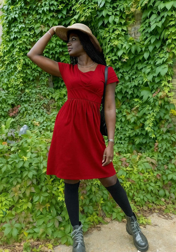 Woman in a red breastfeeding dress standing against a green ivy-covered wall