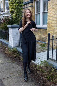 Woman showing her breastfeeding friendly dress on her black midi dress stood in the street.