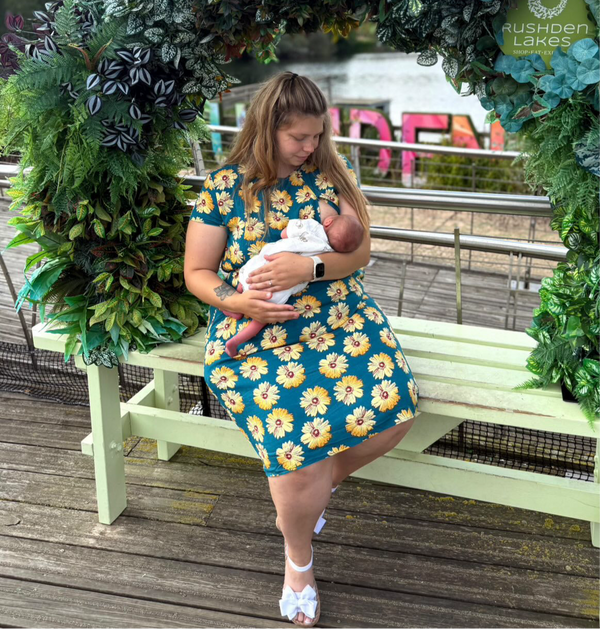 Woman in the a sunflower breastfeeding dress breastfeeding her baby showing the easy access zips for breastfeeding. 