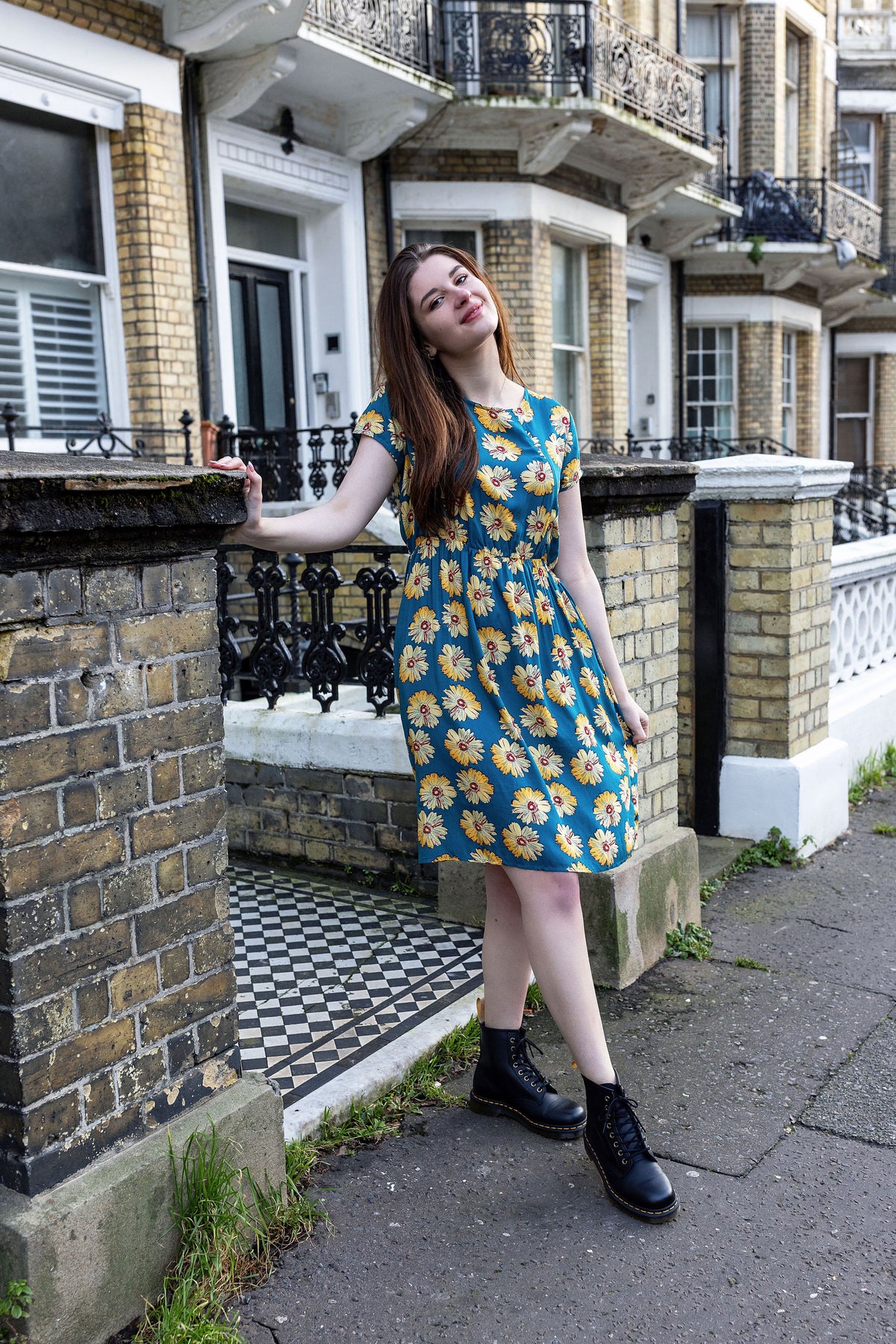 Woman in a blue floral breastfeeding dress standing on a street with a building in the background