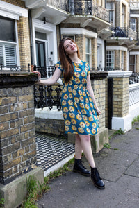 Woman in a blue floral breastfeeding dress standing on a street with a building in the background