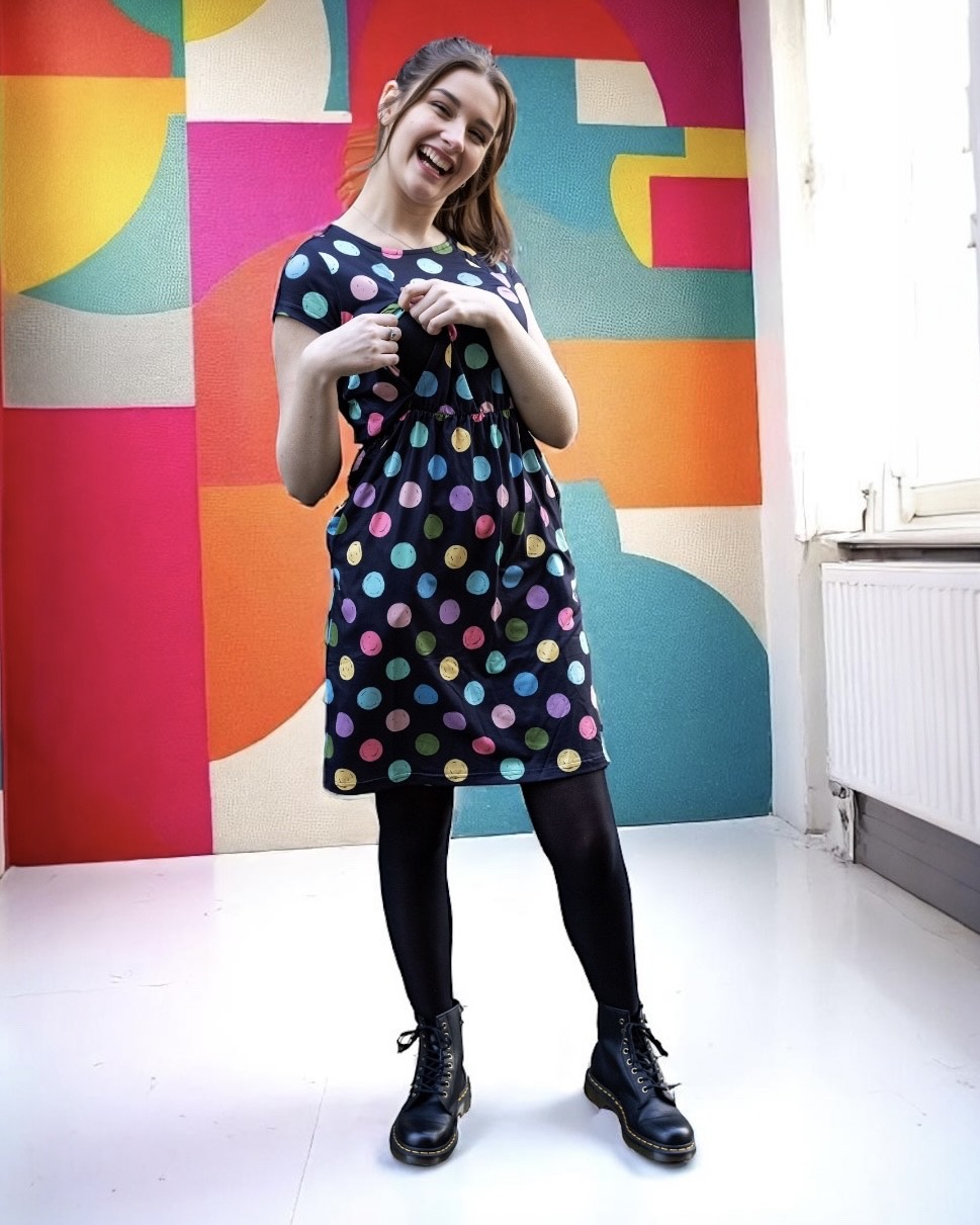 Woman wearing a polka dot breastfeeding dress in front of a geometric wall.