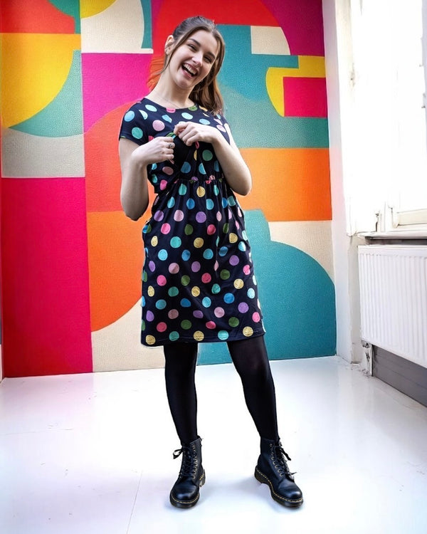 Woman wearing a polka dot breastfeeding dress in front of a geometric wall.