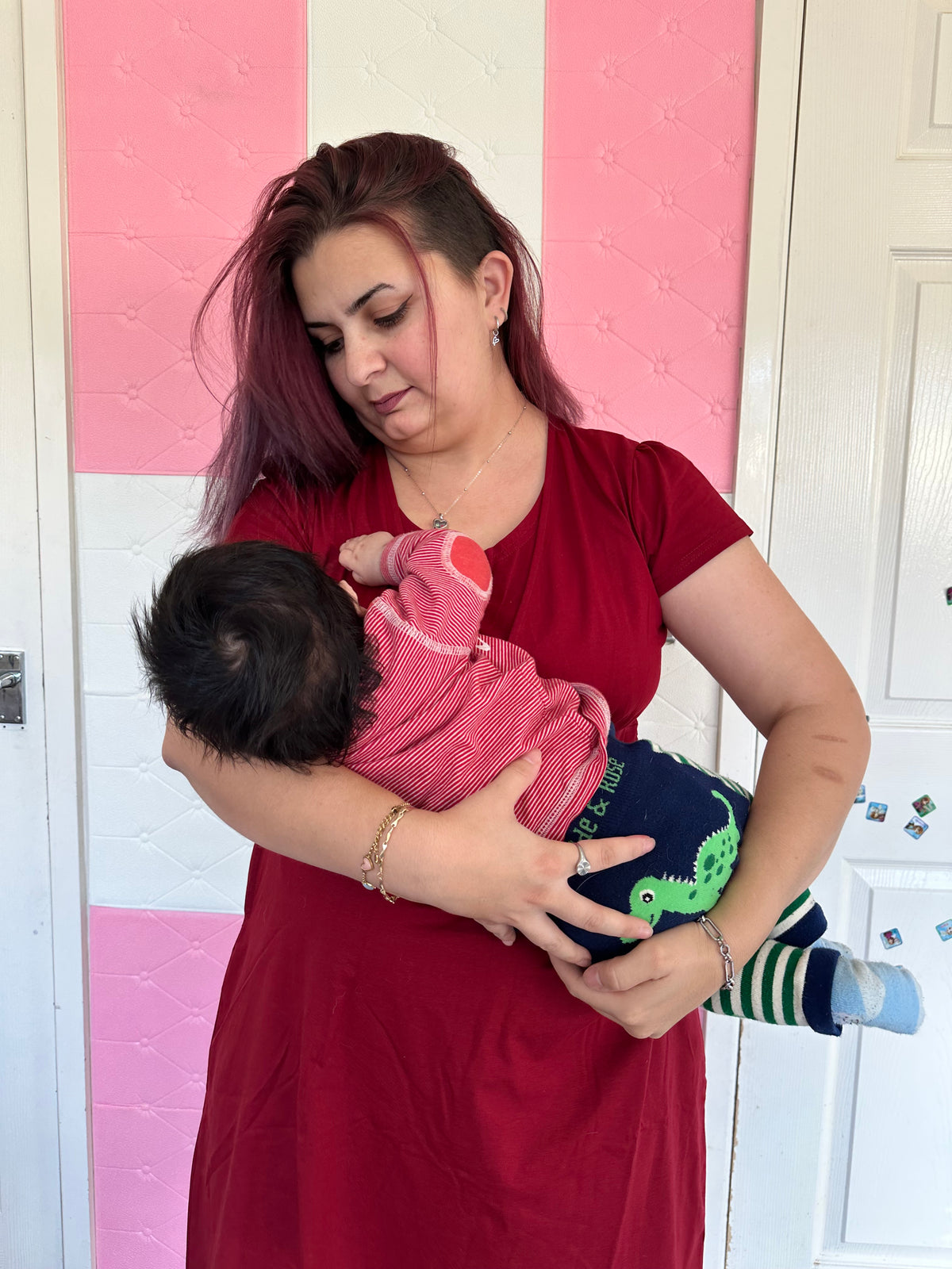 Woman breastfeeding a child on a pink and white checkered floor in a red breastfeeding dress 