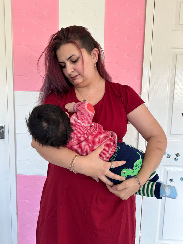 Woman breastfeeding a child on a pink and white checkered floor in a red breastfeeding dress 