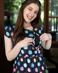 Woman wearing a navy breastfeeding dress with colorful polka dots, smiling outdoors.