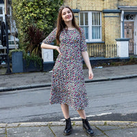 Stylish Mum with hand on hip with rainbow leopard print breastfeeding dress. She has long dark here and is posing confidently. She is also black boots and is stood in on a pavement on a street.